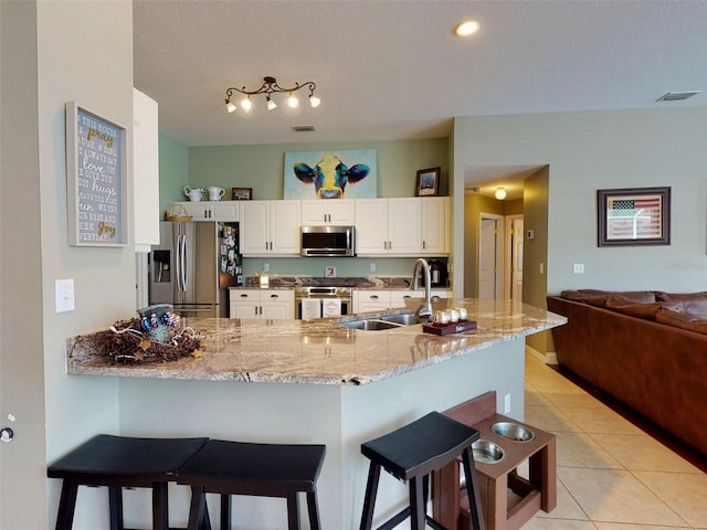 kitchen with kitchen peninsula, sink, white cabinetry, appliances with stainless steel finishes, and light tile patterned floors