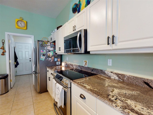 kitchen with white cabinetry, light tile patterned floors, stainless steel appliances, and dark stone counters