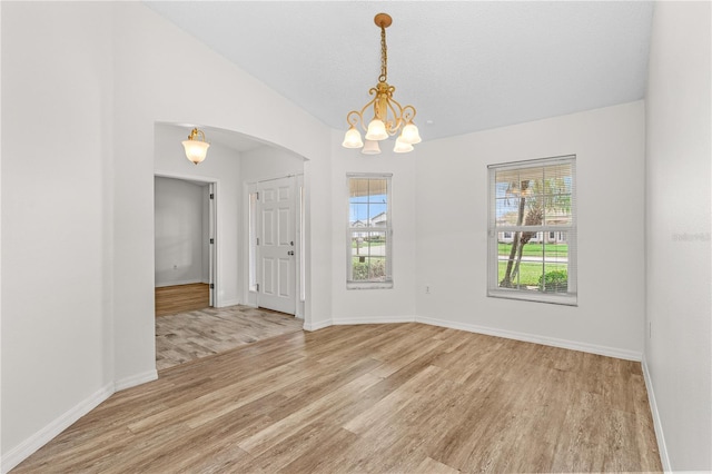 empty room featuring vaulted ceiling, light hardwood / wood-style flooring, and a notable chandelier