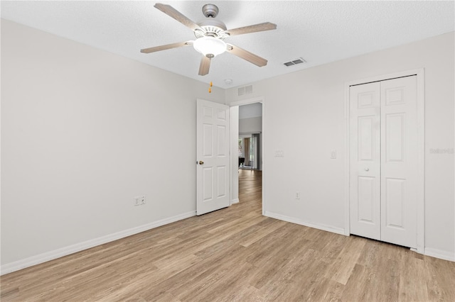 unfurnished bedroom featuring ceiling fan, a closet, light hardwood / wood-style floors, and a textured ceiling