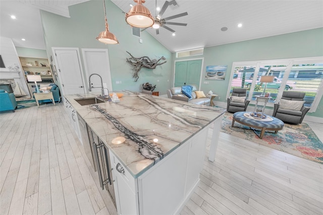 kitchen featuring white cabinetry, sink, a stone fireplace, light stone counters, and pendant lighting