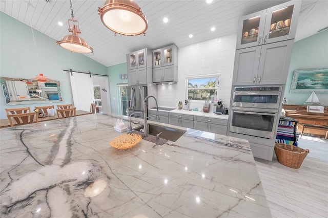 kitchen with a barn door, light stone countertops, gray cabinetry, and stainless steel appliances