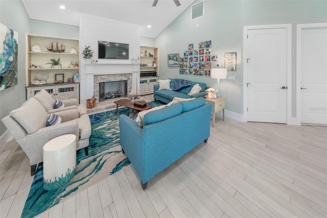 living room featuring ceiling fan, light hardwood / wood-style floors, a fireplace, and built in shelves