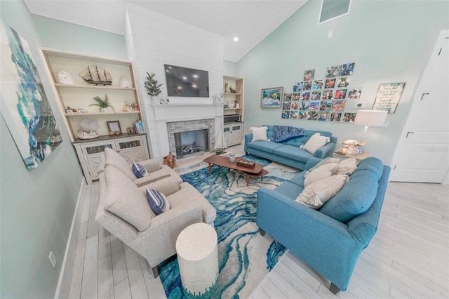 living room featuring a fireplace, high vaulted ceiling, light hardwood / wood-style floors, and built in features