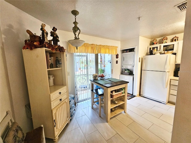 kitchen with pendant lighting, white refrigerator, a textured ceiling, and stacked washer / dryer