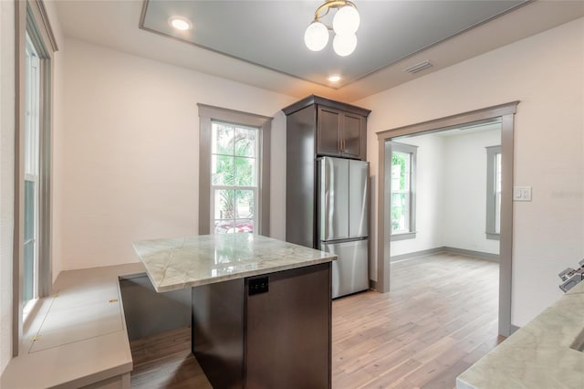 kitchen featuring stainless steel refrigerator, light stone counters, dark brown cabinets, and light wood-type flooring