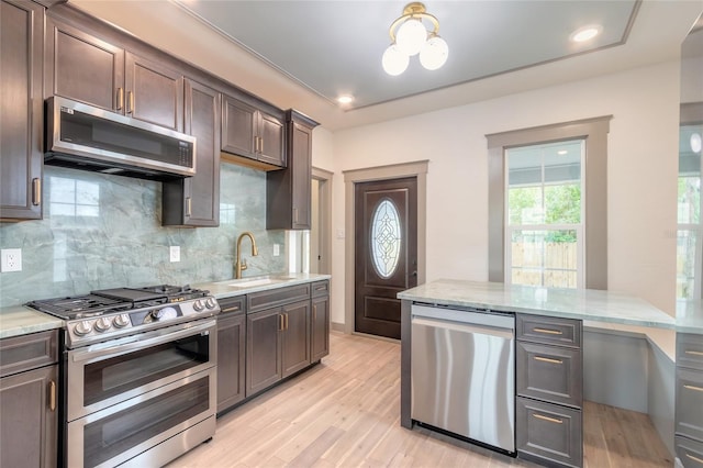 kitchen with backsplash, light stone counters, stainless steel appliances, sink, and light hardwood / wood-style flooring