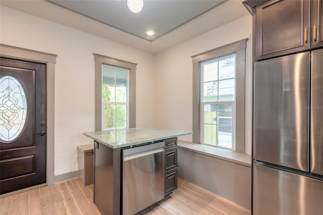 kitchen with a center island, light stone countertops, appliances with stainless steel finishes, dark brown cabinets, and light hardwood / wood-style floors