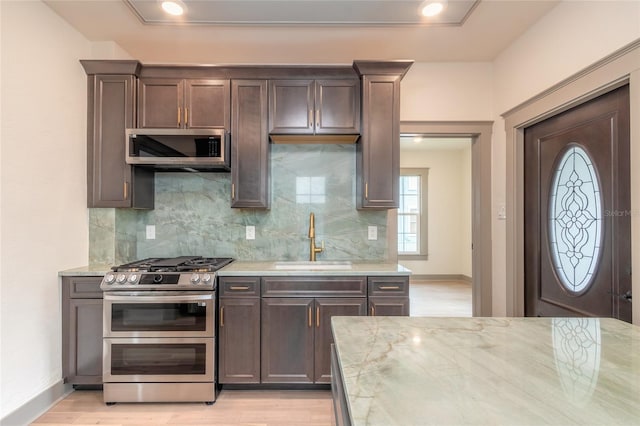 kitchen with light stone counters, sink, appliances with stainless steel finishes, and light hardwood / wood-style flooring