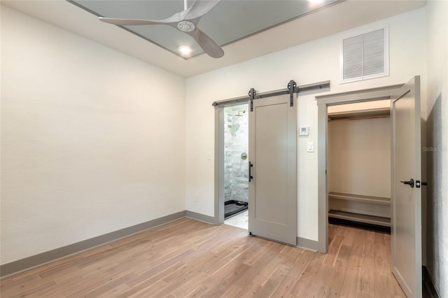 unfurnished bedroom with a barn door, ceiling fan, a closet, and light hardwood / wood-style floors