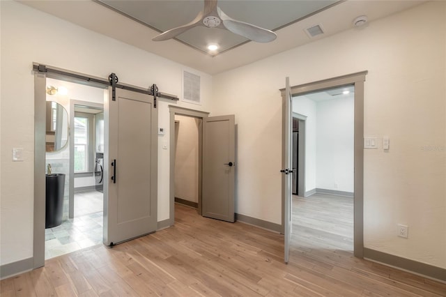 unfurnished bedroom with light wood-type flooring, a barn door, and ceiling fan