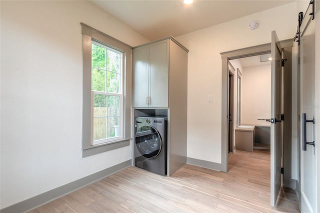 laundry area with cabinets, a barn door, washer / clothes dryer, and light hardwood / wood-style flooring