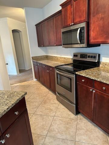 kitchen with light stone countertops, light tile patterned flooring, ornamental molding, and appliances with stainless steel finishes