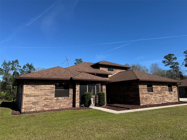 view of front of home featuring brick siding, a front yard, and roof with shingles