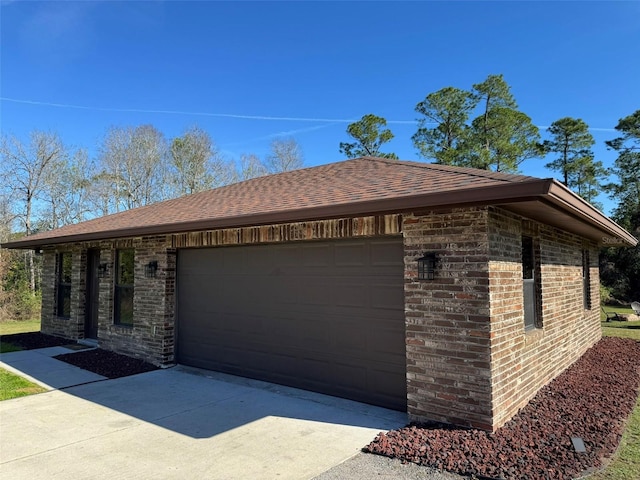 view of side of property with a garage, brick siding, driveway, and roof with shingles