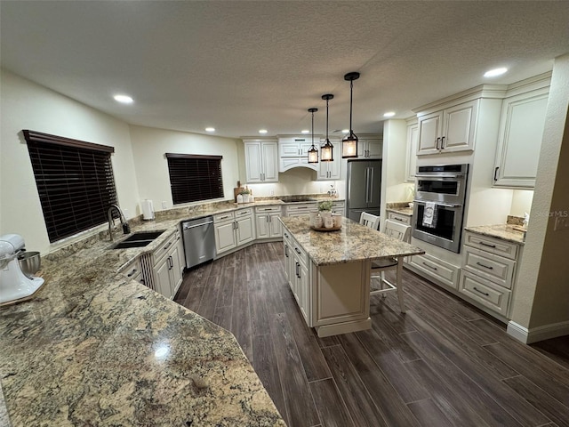 kitchen with sink, a breakfast bar area, decorative light fixtures, appliances with stainless steel finishes, and a kitchen island