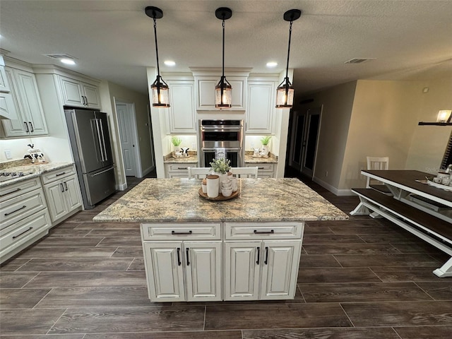 kitchen featuring pendant lighting, appliances with stainless steel finishes, light stone counters, and a kitchen island