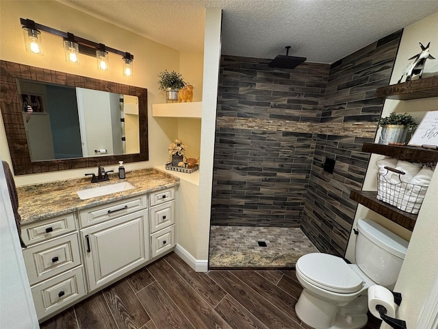 bathroom featuring vanity, toilet, a textured ceiling, and tiled shower