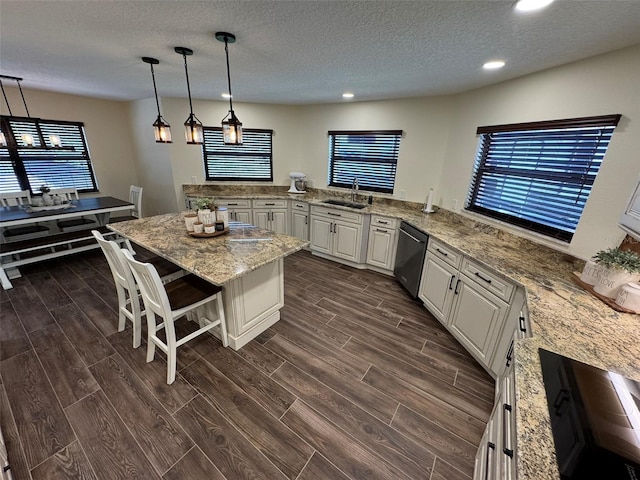 kitchen featuring a kitchen island, wood tiled floor, stainless steel dishwasher, white cabinetry, and a sink