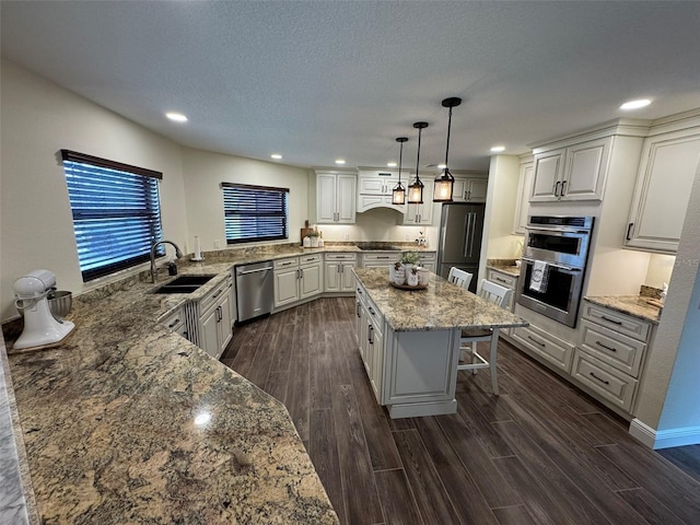 kitchen featuring light stone countertops, wood tiled floor, a sink, stainless steel appliances, and a kitchen breakfast bar