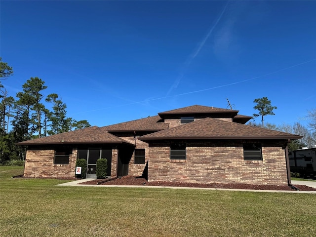 rear view of house with a lawn, roof with shingles, and brick siding