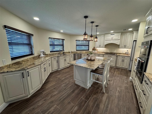 kitchen with a sink, light stone counters, a center island, stainless steel appliances, and dark wood-style flooring