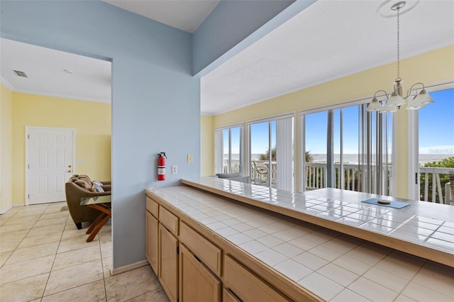 kitchen featuring tile countertops, an inviting chandelier, crown molding, hanging light fixtures, and light tile patterned floors