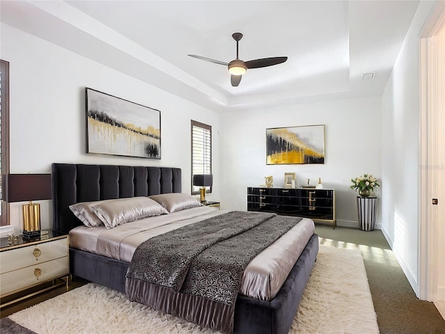 carpeted bedroom featuring a tray ceiling and ceiling fan