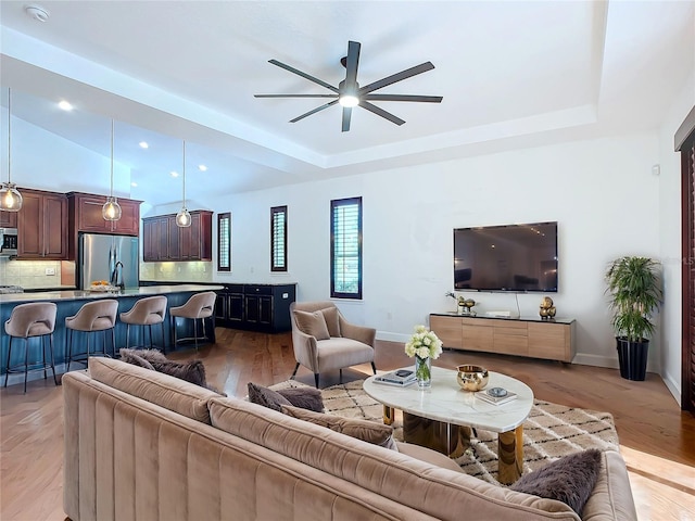 living room featuring a tray ceiling, ceiling fan, and light hardwood / wood-style floors