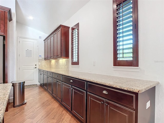 interior space with backsplash, light hardwood / wood-style floors, stainless steel refrigerator, and lofted ceiling