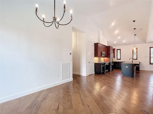 kitchen featuring dark hardwood / wood-style flooring, stainless steel appliances, a kitchen island with sink, hanging light fixtures, and lofted ceiling