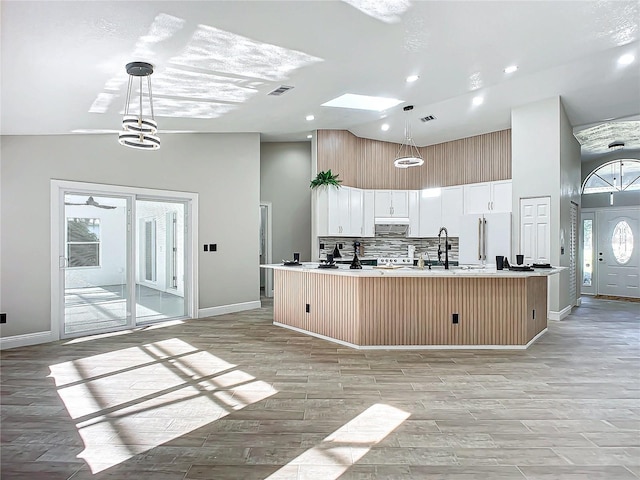 kitchen featuring a center island with sink, hanging light fixtures, high vaulted ceiling, white cabinets, and light hardwood / wood-style flooring