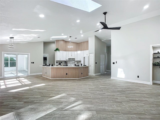 kitchen featuring a center island with sink, a skylight, pendant lighting, high end fridge, and white cabinetry