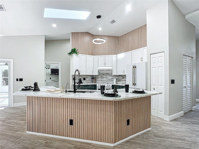 kitchen with high end refrigerator, a kitchen island with sink, a skylight, and white cabinets