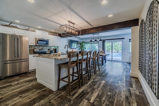 kitchen featuring white cabinets, appliances with stainless steel finishes, beam ceiling, and a kitchen island with sink