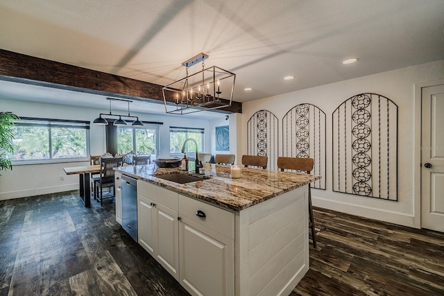 kitchen with sink, white cabinets, light stone counters, an island with sink, and beamed ceiling