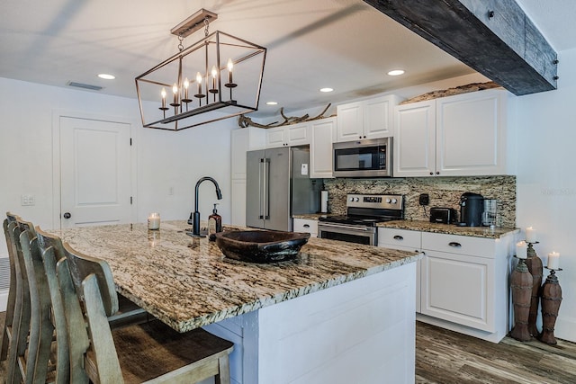 kitchen with white cabinets, stainless steel appliances, a kitchen island with sink, and decorative light fixtures