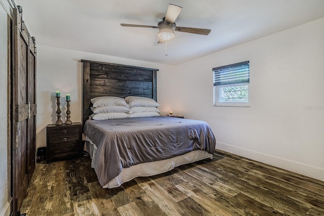 bedroom featuring dark hardwood / wood-style floors, ceiling fan, and a barn door