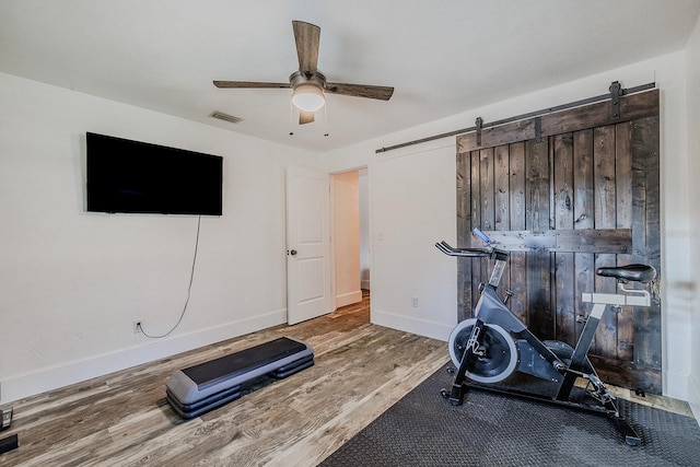 exercise area with ceiling fan, a barn door, and hardwood / wood-style floors