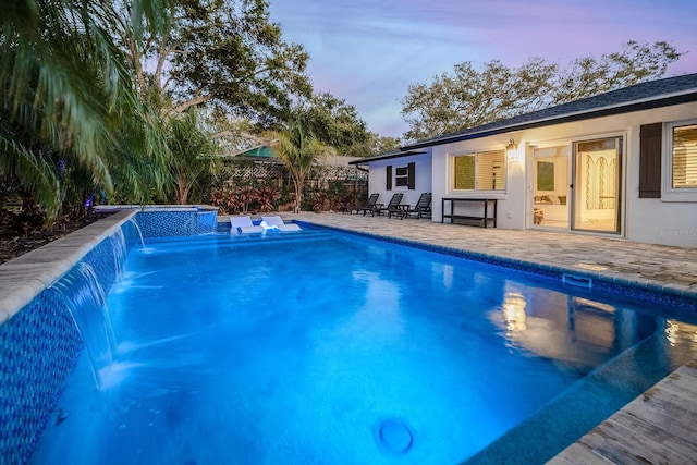 pool at dusk with pool water feature, a patio area, and a jacuzzi