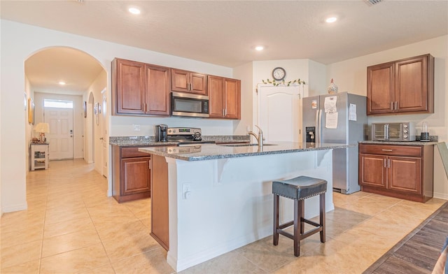 kitchen with a kitchen breakfast bar, sink, dark stone countertops, an island with sink, and stainless steel appliances