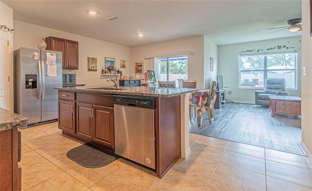 kitchen with appliances with stainless steel finishes, a kitchen island with sink, sink, dark stone countertops, and light tile patterned flooring