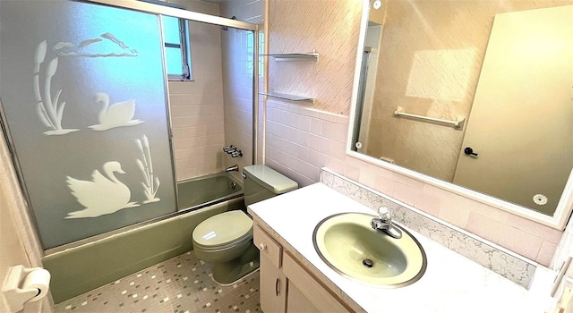 full bathroom with vanity, bath / shower combo with glass door, tile walls, and toilet