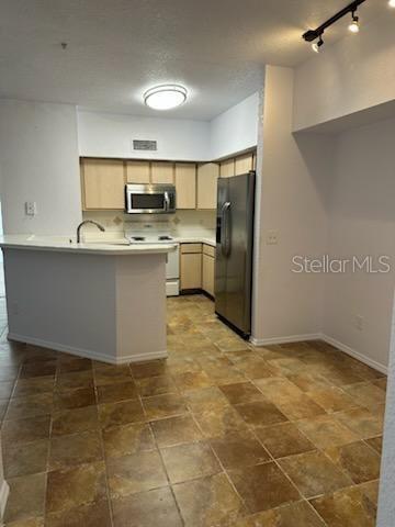 kitchen with sink, light brown cabinets, kitchen peninsula, a kitchen bar, and appliances with stainless steel finishes