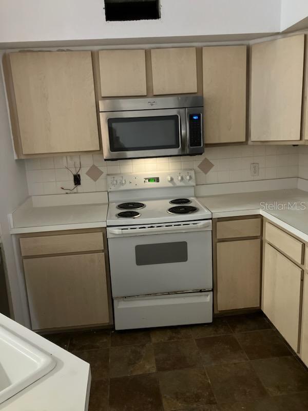 kitchen with light brown cabinetry, backsplash, and white electric stove