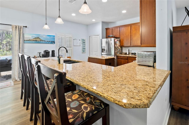 kitchen featuring stainless steel fridge with ice dispenser, light stone countertops, sink, and decorative light fixtures