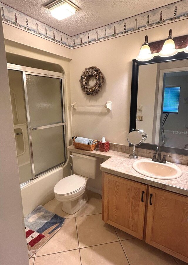 full bathroom with tile patterned flooring, bath / shower combo with glass door, a textured ceiling, toilet, and vanity