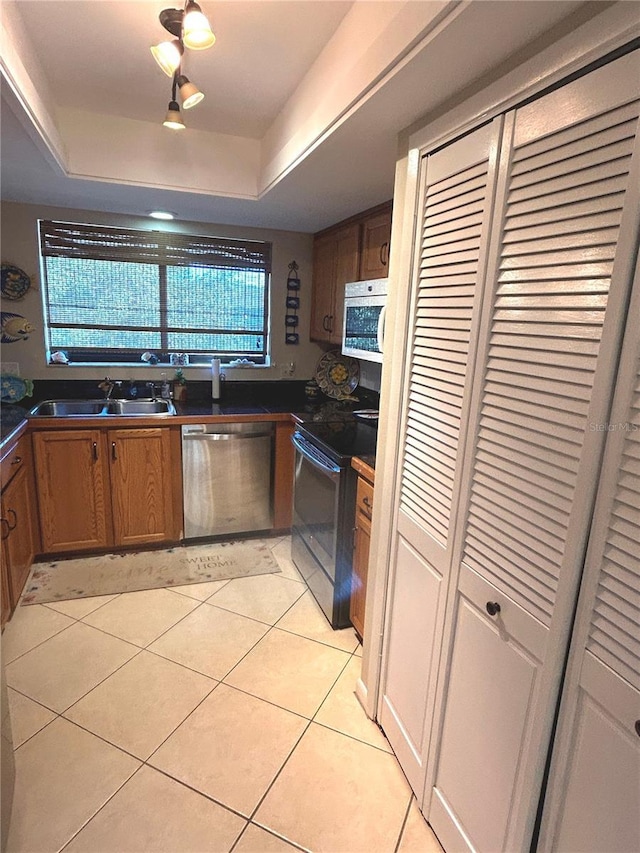 kitchen with a raised ceiling, sink, light tile patterned floors, and stainless steel appliances