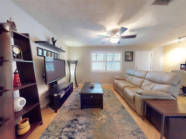 living room with a textured ceiling, light hardwood / wood-style flooring, and ceiling fan