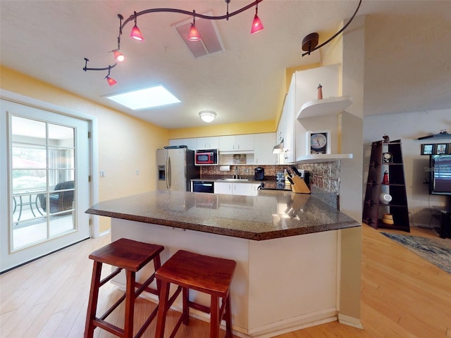 kitchen with a skylight, stainless steel fridge with ice dispenser, kitchen peninsula, light hardwood / wood-style floors, and white cabinets